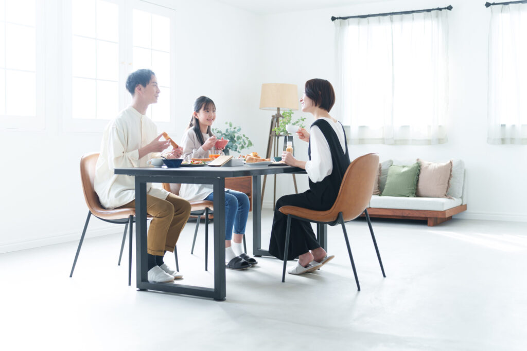 ソファまでひと続きの明るいダイニングで朝食をとるご家族（デモ）