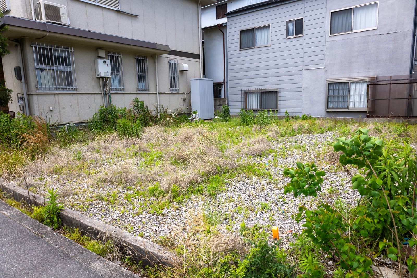 住宅地にある更地の敷地。奥に既存の建物が並ぶ（デモ）